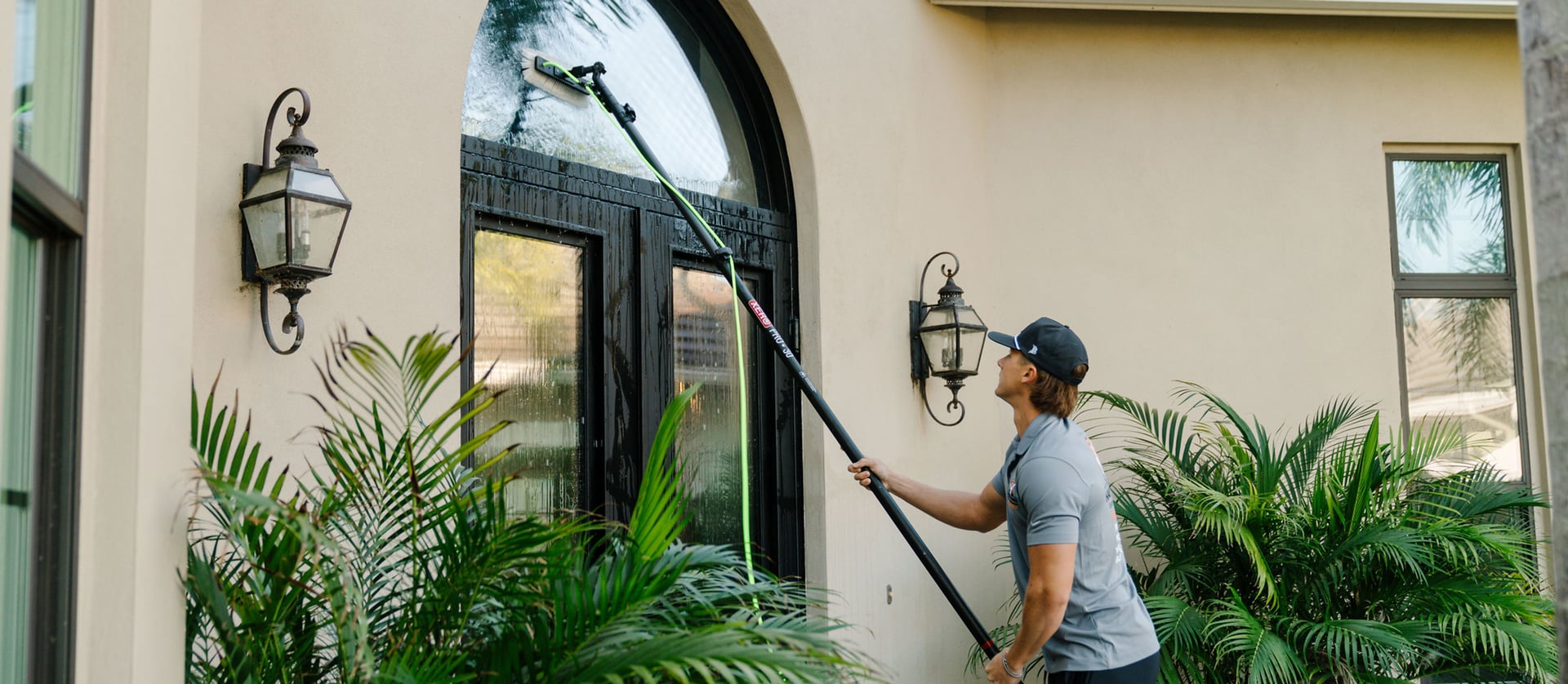 Technician cleaning a large arched window with a water-fed pole